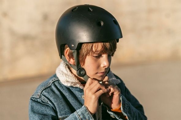 Barn spänner fast ett svart cykelhjälm före cykling